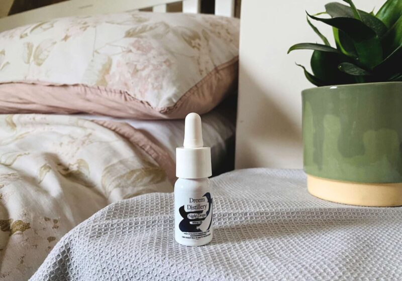 A bottle of Dreem Distillery CBD oil night drops next to a bed